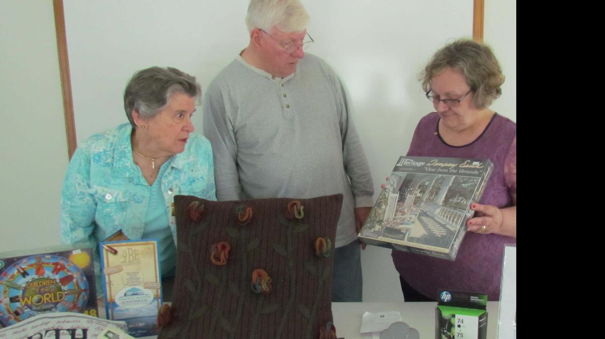
Yvonne Moody (from left) and Matthew Ernst, volunteers with the Brunswick County Literacy Council, and Dorothy Hoerr, executive director of the literacy council, arrange items donated to the A to Z Silent Auction to accompany the Adult Spelling Bee Monday. 
