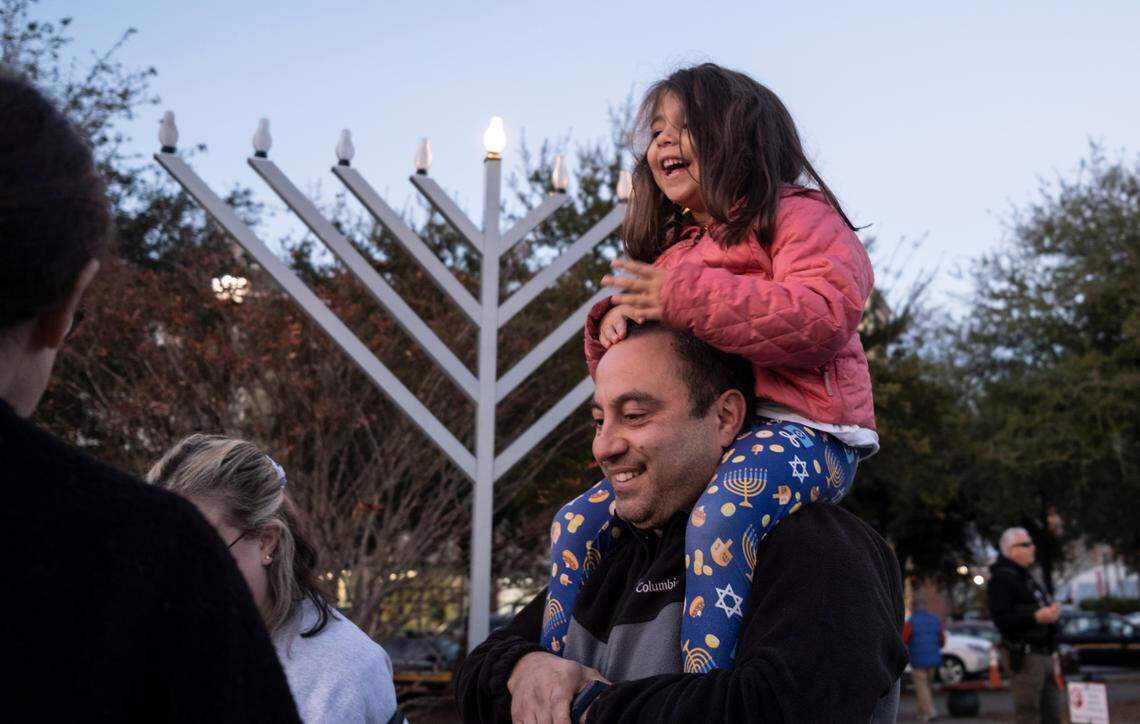 Four-year-old Shira Shirt sits on Felix Shoihat’s shoulders as they greet friends at a Menorah lighting at Valor Park in Myrtle Beach.