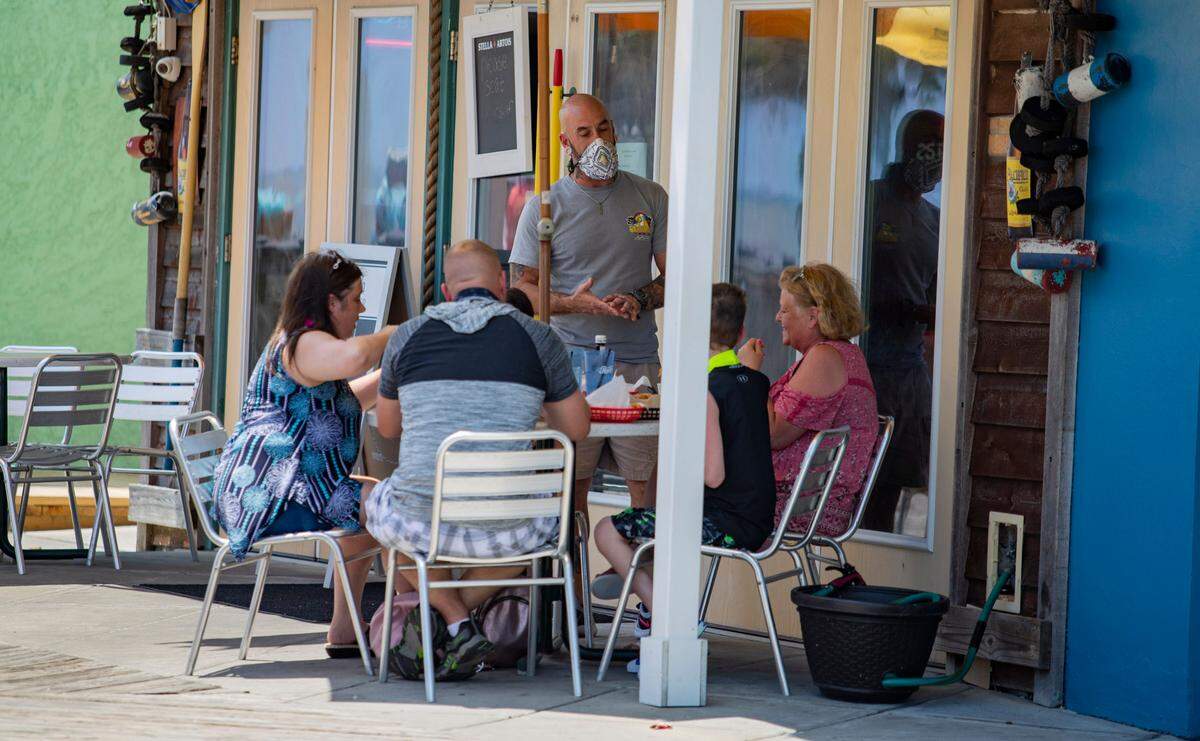A masked server speaks with a table at Dirty Don’s Oyster Bar & Grill along the Myrtle Beach boardwalk.
