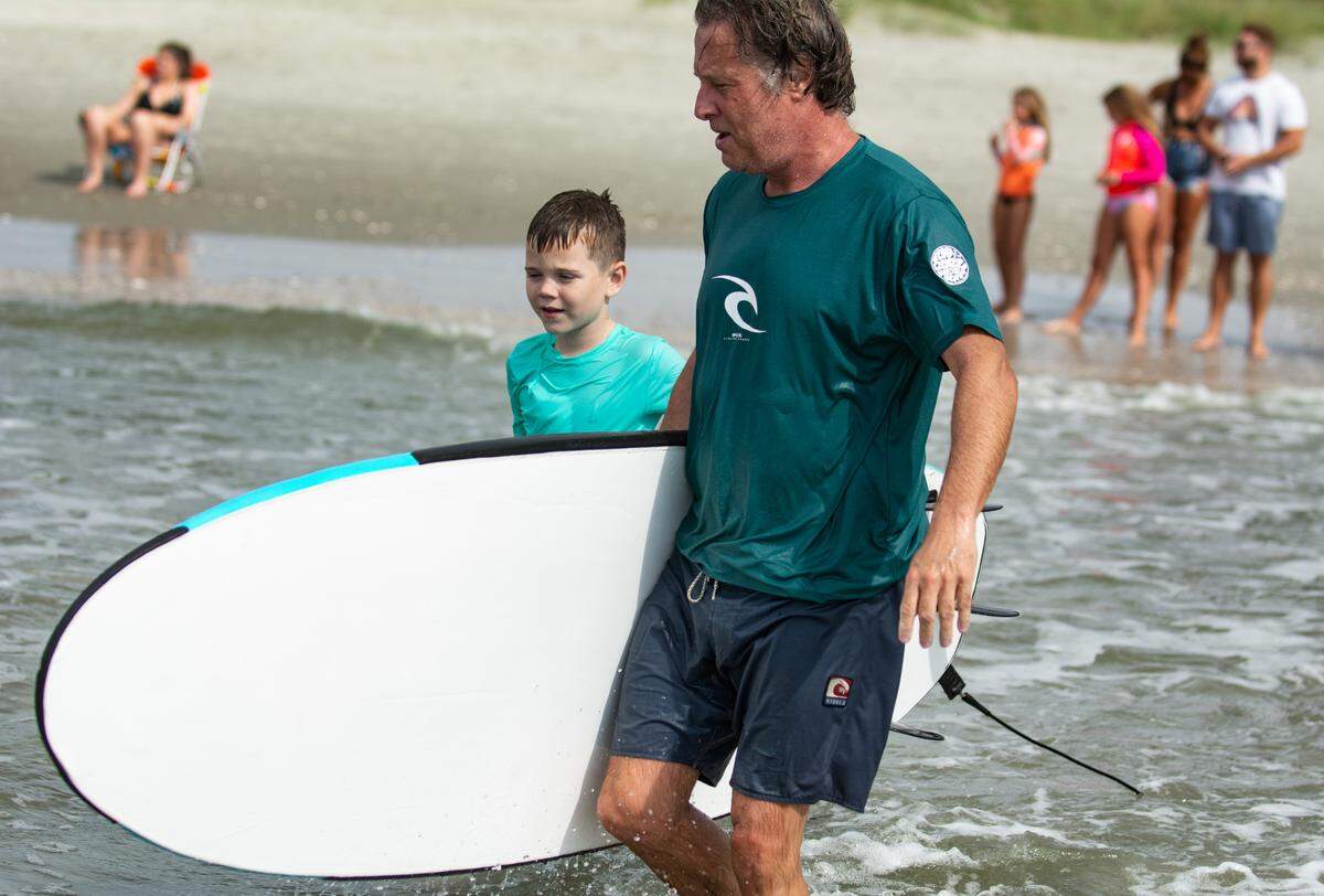 Event director Tyler Watkins takes Logan Herlihy, 9, out for Take A Kid Surfing Day in North Myrtle Beach on Aug. 7, 2021.