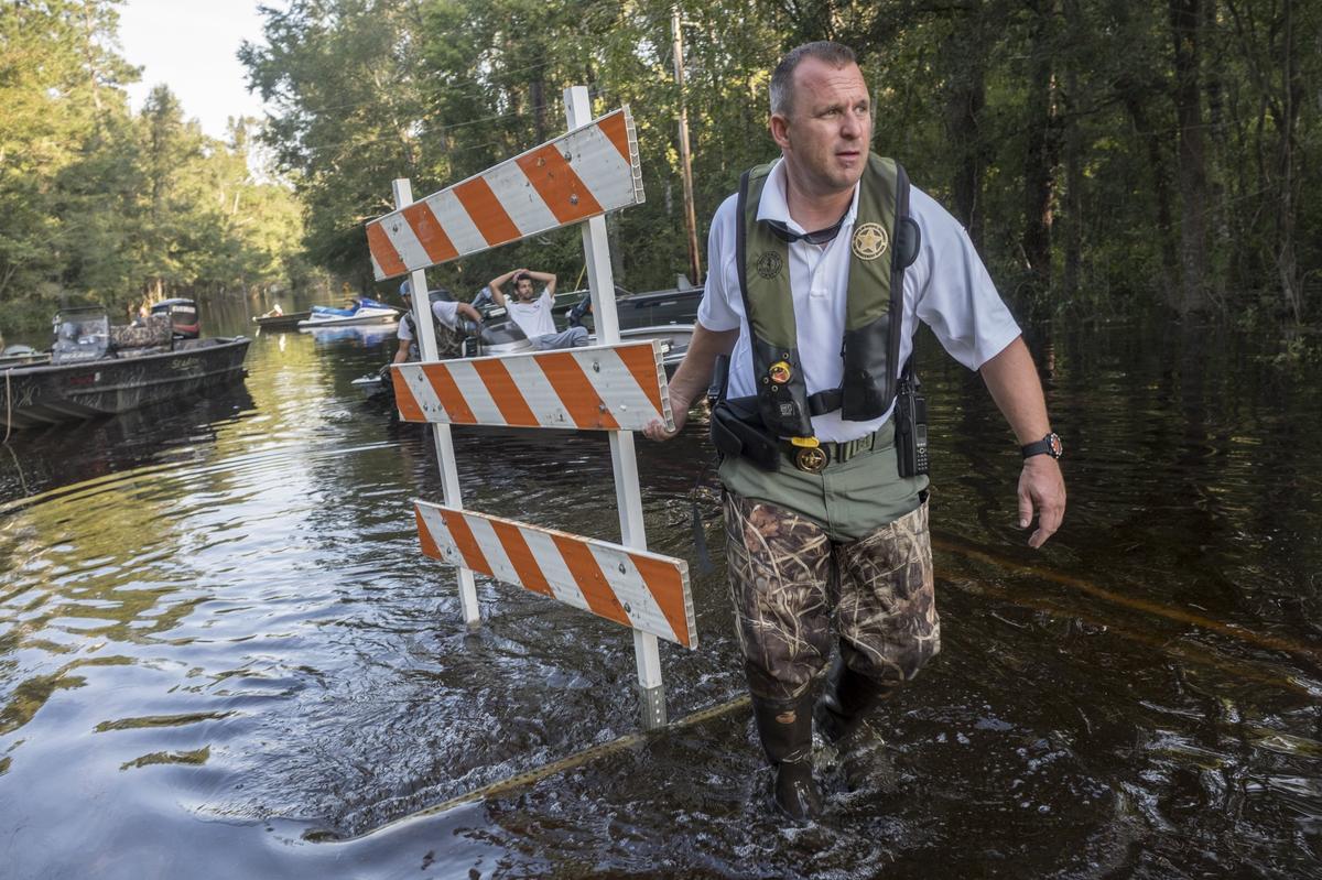 SCDNR’s LCpl. Ezra Arnold moves the road barricade sign to higher ground as flood waters continue to rise to near historical levels at Lee’s Landing near Conway. Friday, September 21, 2018.