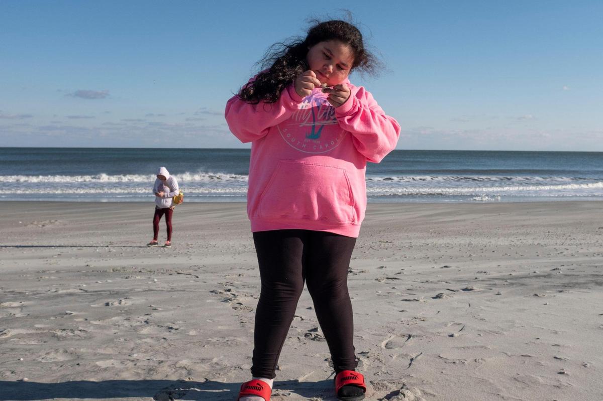 Faith Ruiz, 8, looks closely at a shell she picked up on the beach. Faith has Bardet-Biedl Syndrome, a rare genetic disorder linked to childhood obesity and vision problems with most of those afflicted going legally blind by age 15. January 28, 2021.
