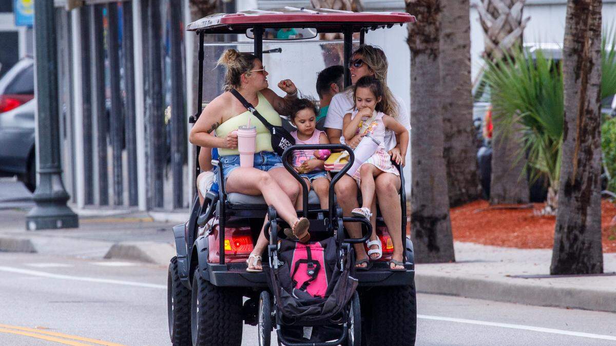 A family pulls their stroller behind a golf cart on Ocean Boulevard on Monday. The week of July 4th is one of the times for tourism in the Myrtle Beach area. July 1, 2024.