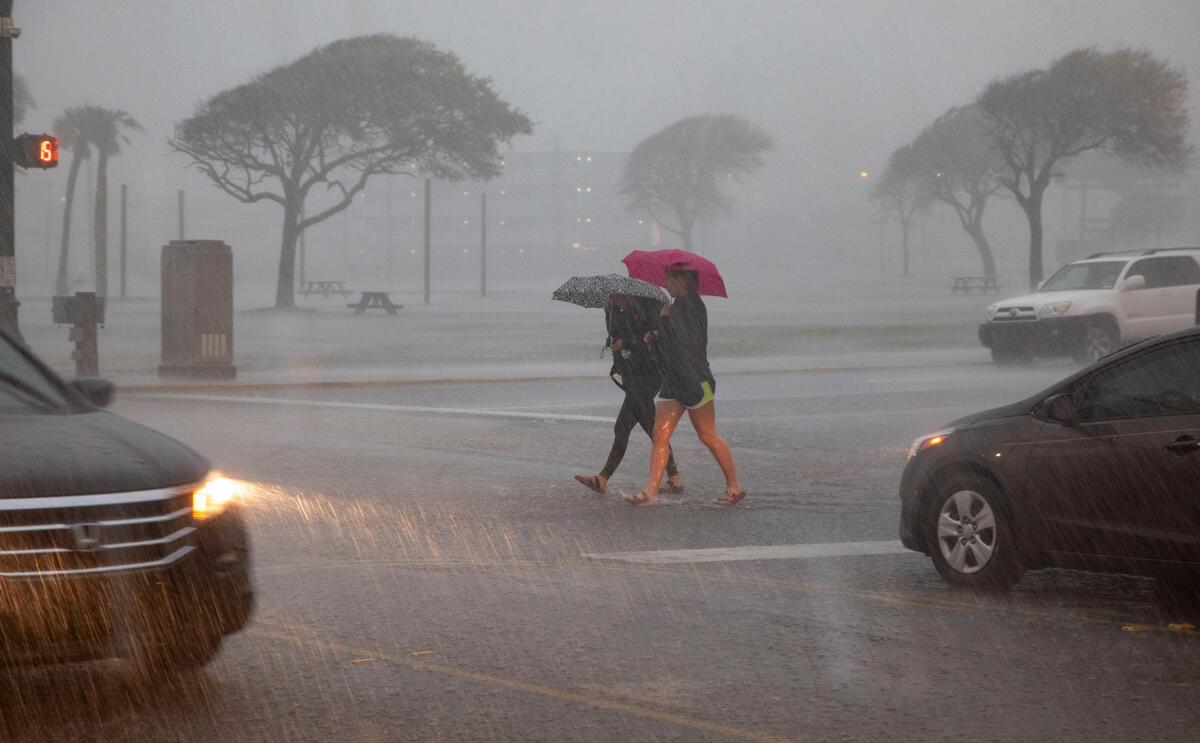 Pedestrians battle wind and rain as they cross over Ocean Boulevard to the Myrtle Beach Boardwalk Friday morning.
