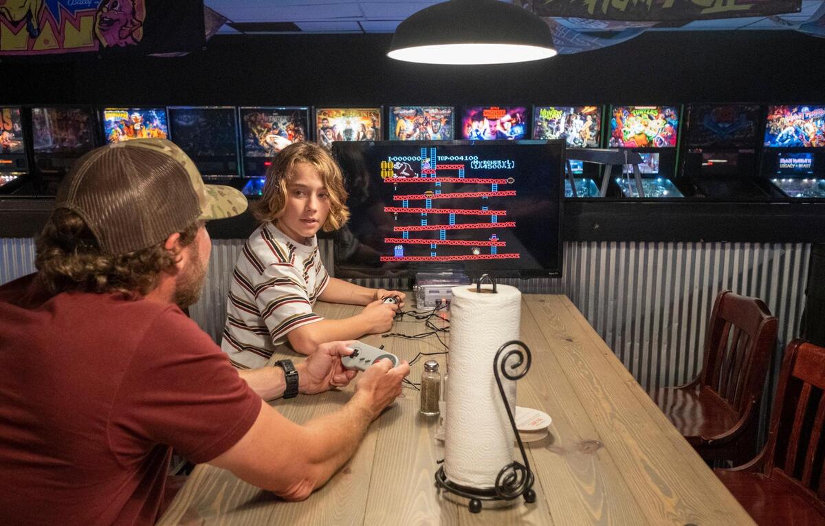 Tyler McCullough plays arcade games with his father Brandon McCullough while sitting at a pub table at The Player 1UP arcade bar that has opened in Murrells Inlet. The bar features classic coin operated arcade games that date back to the early 1980s, pinball machines, billiards tables, air hockey, Skee-Ball, NBA Hoops, racing games and shooting games. It also has a rooftop bar. May 13, 2022.