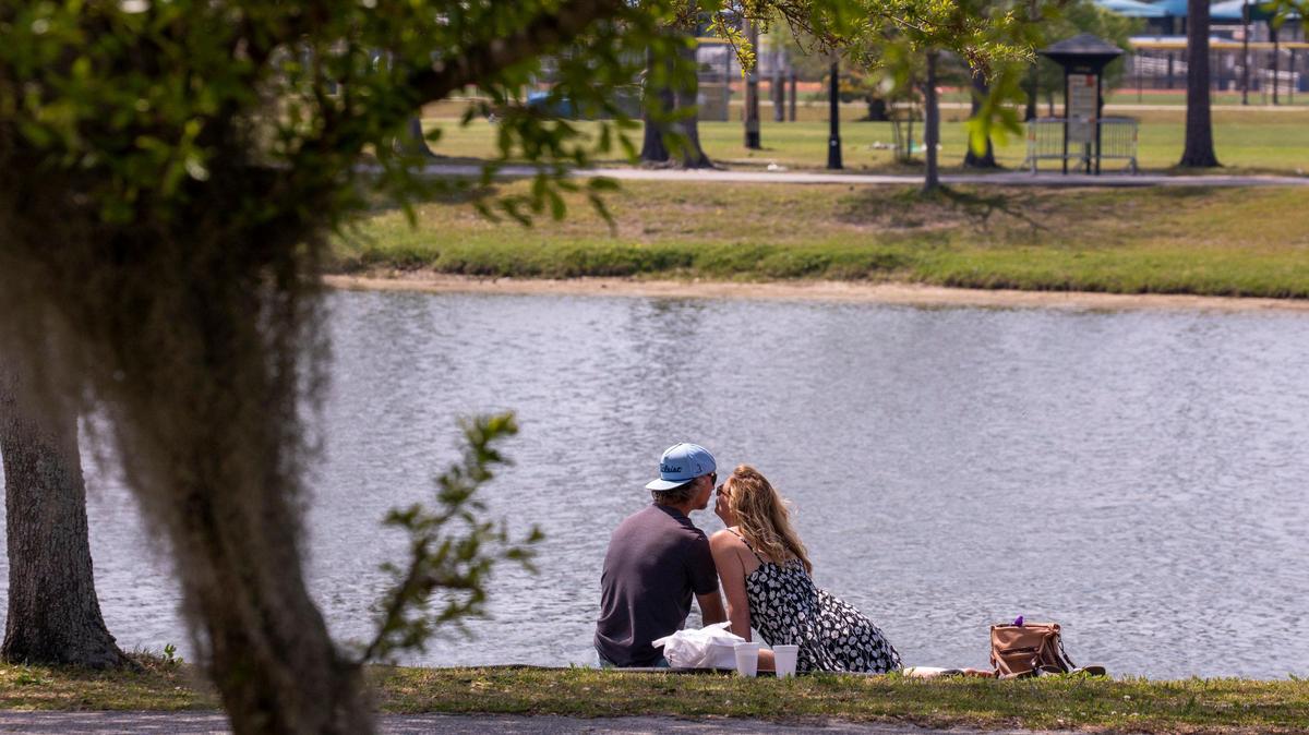 A couple sits on the grass for a picnic lunch beside the Market Common Grand Lake. April 7, 2020