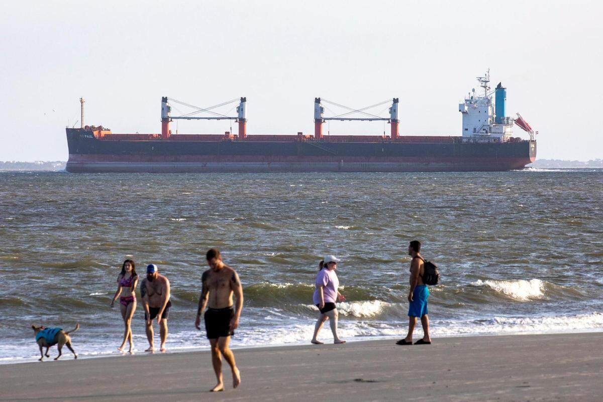 A ship passes through Charleston harbor as beachgoers walk Sullivan’s Island. Shifting sands are having opposite effects on some Charleston area beaches with erosion claiming the Folly Beach shoreline while Sullivan Island’s beach is growing. July 21, 2022.