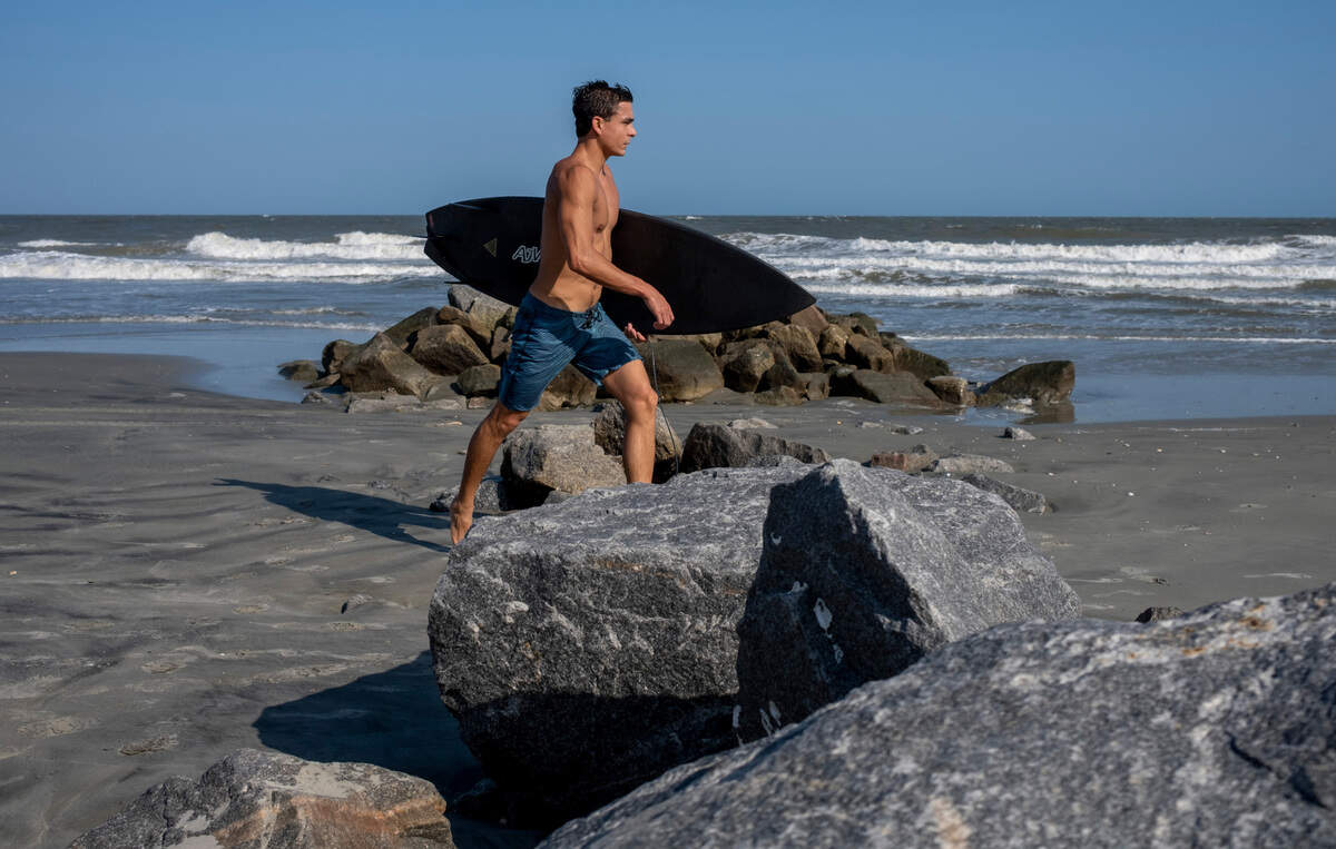 A surfer crosses a rock goin at Folly Beach. Shifting sands are having opposite effects on some Charleston area beaches with erosion claiming the Folly Beach shoreline while Sullivan Island’s beach is growing. July 21, 2022.