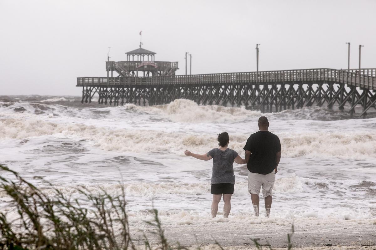 A couple stands in the foamy surf watching as the Cherry Grove Pier is battered by high waves on Thursday. After coming ashore as a category 4 Hurricane in Florida, the remnants of Hurricane Michael passed through the Grand Strand bringing high winds, and coastal flooding on Thursday. Oct. 11, 2018