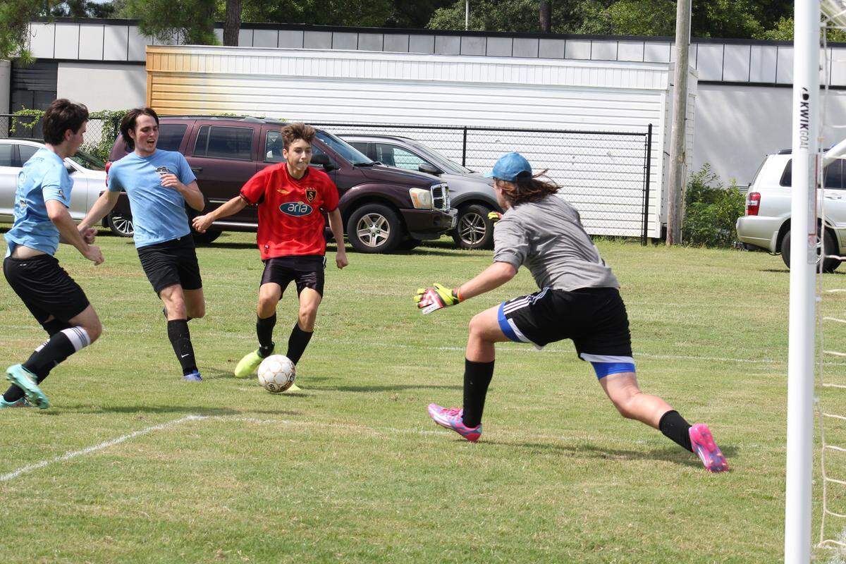 Legends soccer team member Jared Crooks, 16, (in red) takes a shot against Chicago FC goalkeeper Josh Marlow, 18, during a charity soccer tournament raising money to send soccer equipment to kids in Costa Rica and Nigeria. Legends won the game by 7 - 1.