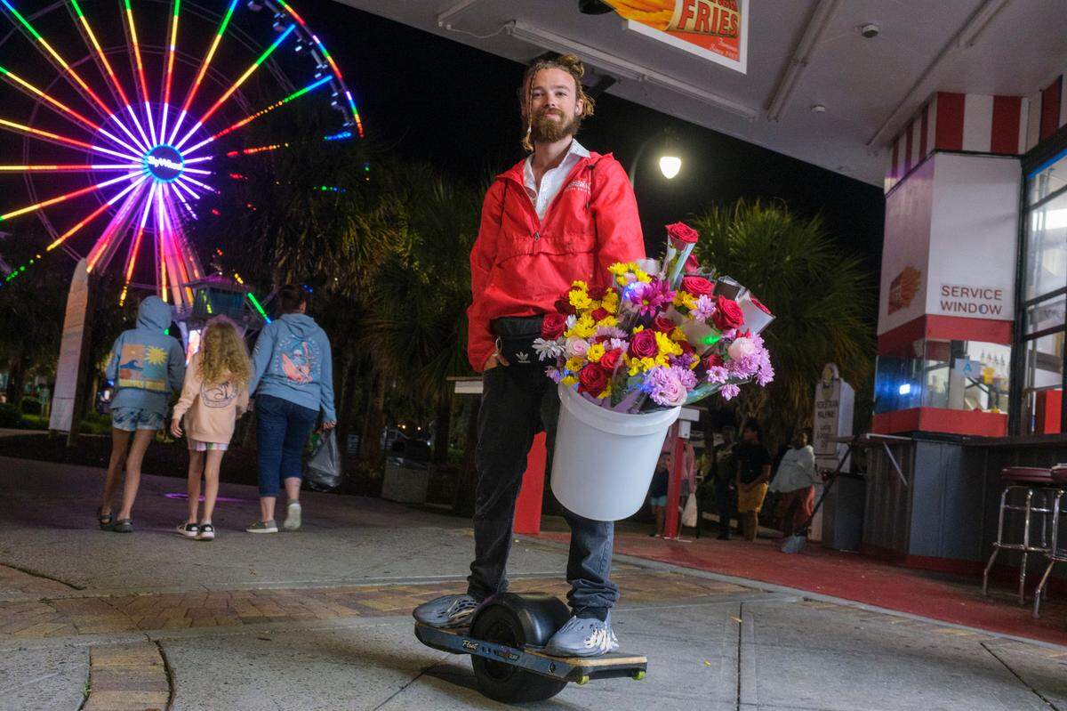 Issac Shinault of Greensboro NC, rides his One Wheel around the downtown area selling flowers to tourist. Shinault was on vacation himself on Friday night be said the saw an opportunity to make a little money. Downtown Myrtle Beach’s tourist district was relatively quiet for a Summer evening on Ocean Boulevard and the Boardwalk. Storms put a damper on the evening activities but as the skies cleared, visitors returned to enjoy the attractions. Friday, May 30, 2025.