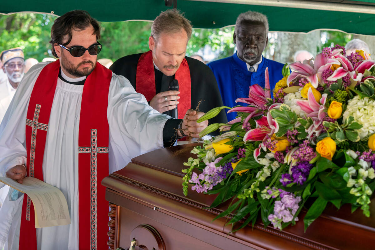 Religious leaders from Holy Cross Faith Memorial Church sprinkle dirt on the coffin holding the remains of 22 enslaved people before it was buried.
