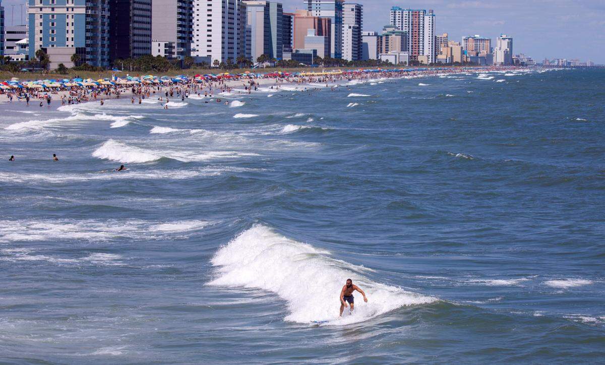 A surfer catches a wave near the Springmaid Pier with the city of Myrtle Beach skyline in the background. The week of July 4th is one of the times for tourism in the Myrtle Beach area. July 2, 2024.