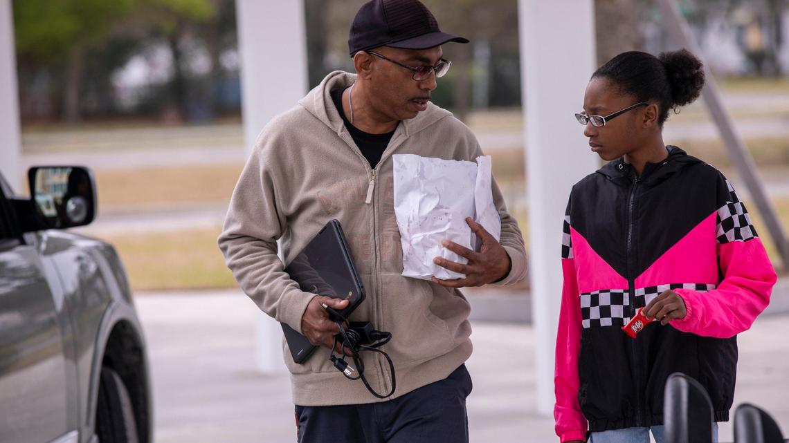 U.L Sharper and his 6-grade daughter Ashley pick up a computer and food from Myrtle Beach Middle School on Wednesday. Students and their families pick up e-learning supplies, including Chromebook computers, binders and band instruments, as well as prepared meals at Myrtle Beach Middle School on the first day of the Horry County Schools distribution program. The Wake County school system is setting up its own computer distribution program.
