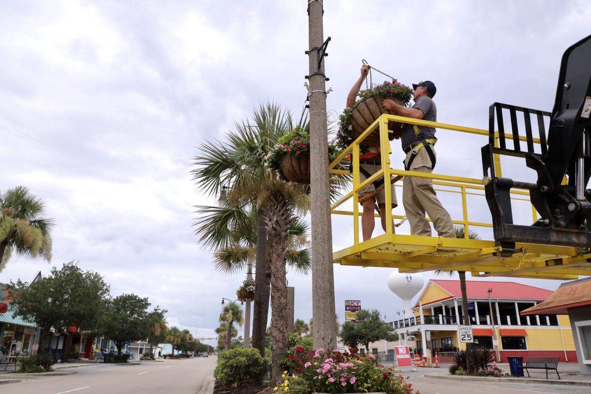 City of North Myrtle Beach workers remove hanging plants from post along Main Street in advance of the storm.