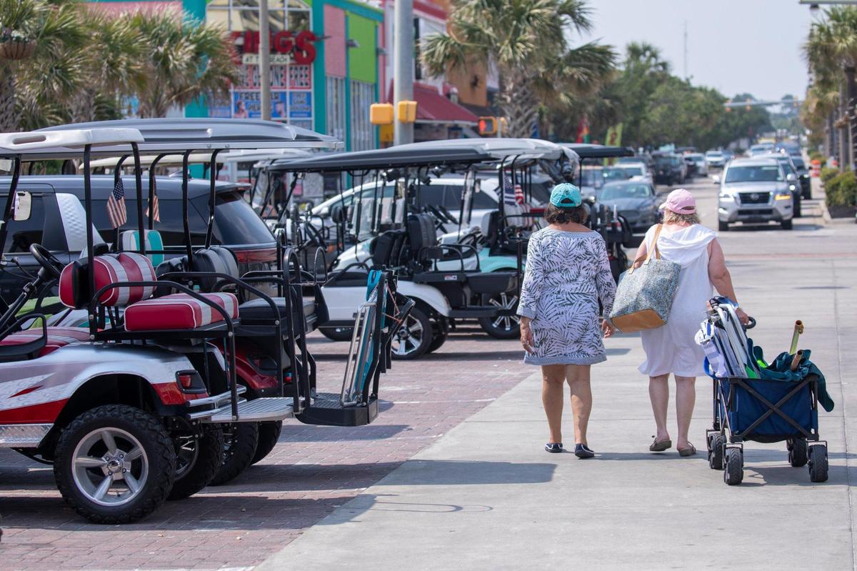 Beach visitors walk past a line of golf carts at the Main Street beach access in North Myrtle Beach, S.C. June 9, 2023.