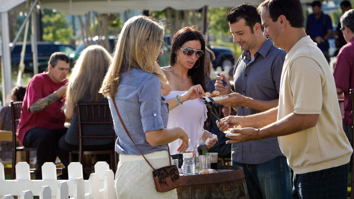 Left to right, Carla Guyton and Ginci Caprio sample items retrieved by their husbands John and Ben. Beautiful weather, a relaxed atmosphere, and scrumptious cuisine at The Taste of Market Common make for a delightful Saturday afternoon in Valor Park. Photo by Matt Silfer for The Sun News.