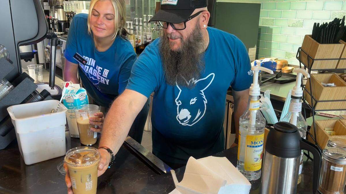Bad Ass Coffee of Hawaii manager Ron “Crash” Kissell serves an iced coffee during the restaurant’s second week of business. The shop uses coffee ice cubes in its drinks to prevent them from becoming watered down. June 23, 2025. 