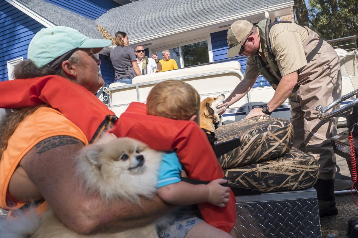 Ian Lundell of SLED calms a dog as Denise Milligan and her grandson 2-year-old Hunter sit in a DNR boat waiting for the rest of her family and belongings to be transported to dry land. As flood waters continue to rise to near historical levels at Lee’s Landing near Conway residents of the Waccamaw River community were making final evacuations with the help of various agencies. Friday, September 21, 2018.