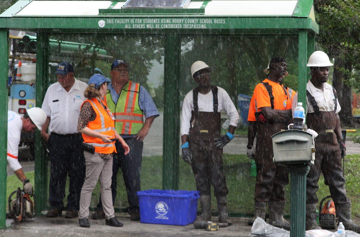 Workers huddle under a bus stop shelter while the rain comes down. City staff were busy repairing a corroded sewer pipe in Myrtle Beach that spilled out more than 100,000 gallons of sewer water Monday morning.