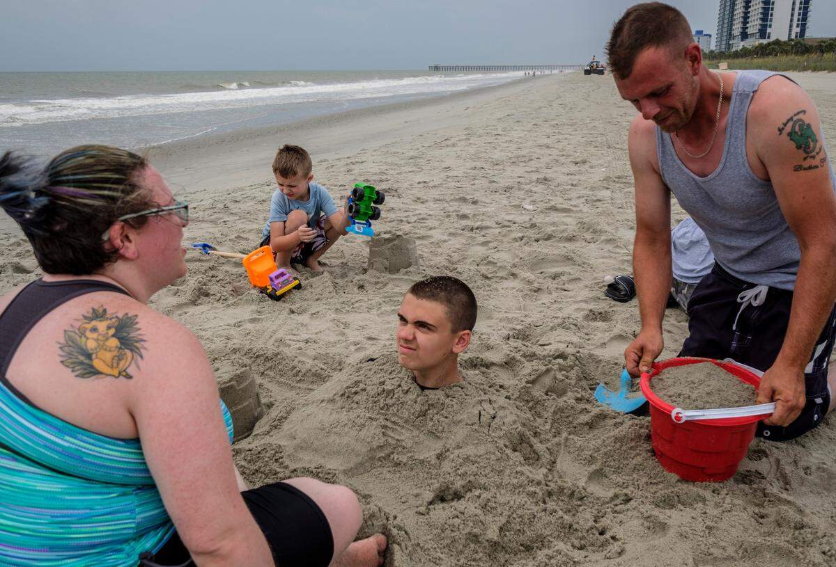 John Blum of Baltimore, M.D., gets buried in the sand by his father Steve Blum as family friends Lliam Pope (7) and Susan Pope watch in Myrtle Beach on Monday. The group said they had little concern about the oncoming storm and planned to continue their vacation. Tropical Storm Isaisas is moving up the east coast and is expected to make landfall near Myrtle Beach on Monday night. August 3, 2020.