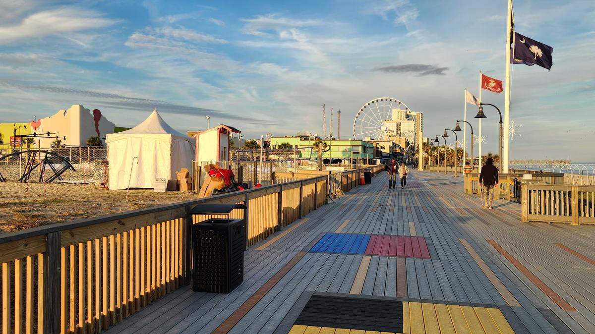 People walk along the boardwalk in Myrtle Beach shortly before sunset on Nov. 16, 2022. The city is planning to install 100 ottoman-style benches in the area.