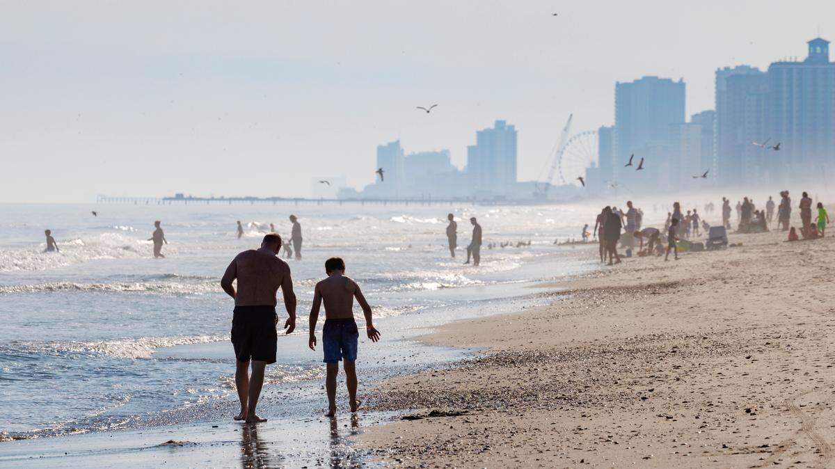People walk the beach and play in the surf on an unseasonably warm February afternoon in Myrtle Beach, S.C. Hazy conditions caused by fires in the area did not deter visitors from enjoying the sun. Feb. 26, 2025
