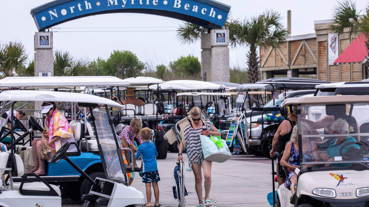 Beachgoers walk between golf carts at the “Horseshoe” in North Myrtle Beach, S.C. On boats, beaches and the boulevards, tourists and residents enjoy the first days of the summer season on the Grand Strand during Memorial Day weekend 2021. May 29, 2021.
