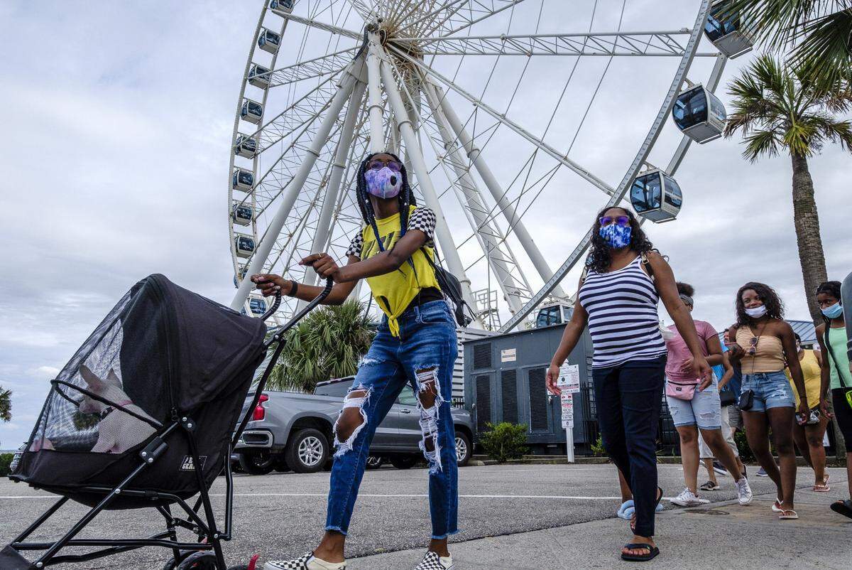 A family wearing masks walk past the Sky Wheel attraction in Myrtle Beach on Tuesday, July 7, 2020.