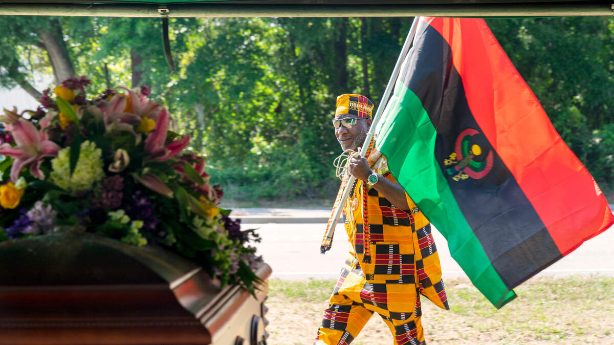 John D. Henry holds an African flag as he walks by the coffin holding the remains of 22 enslaved people.