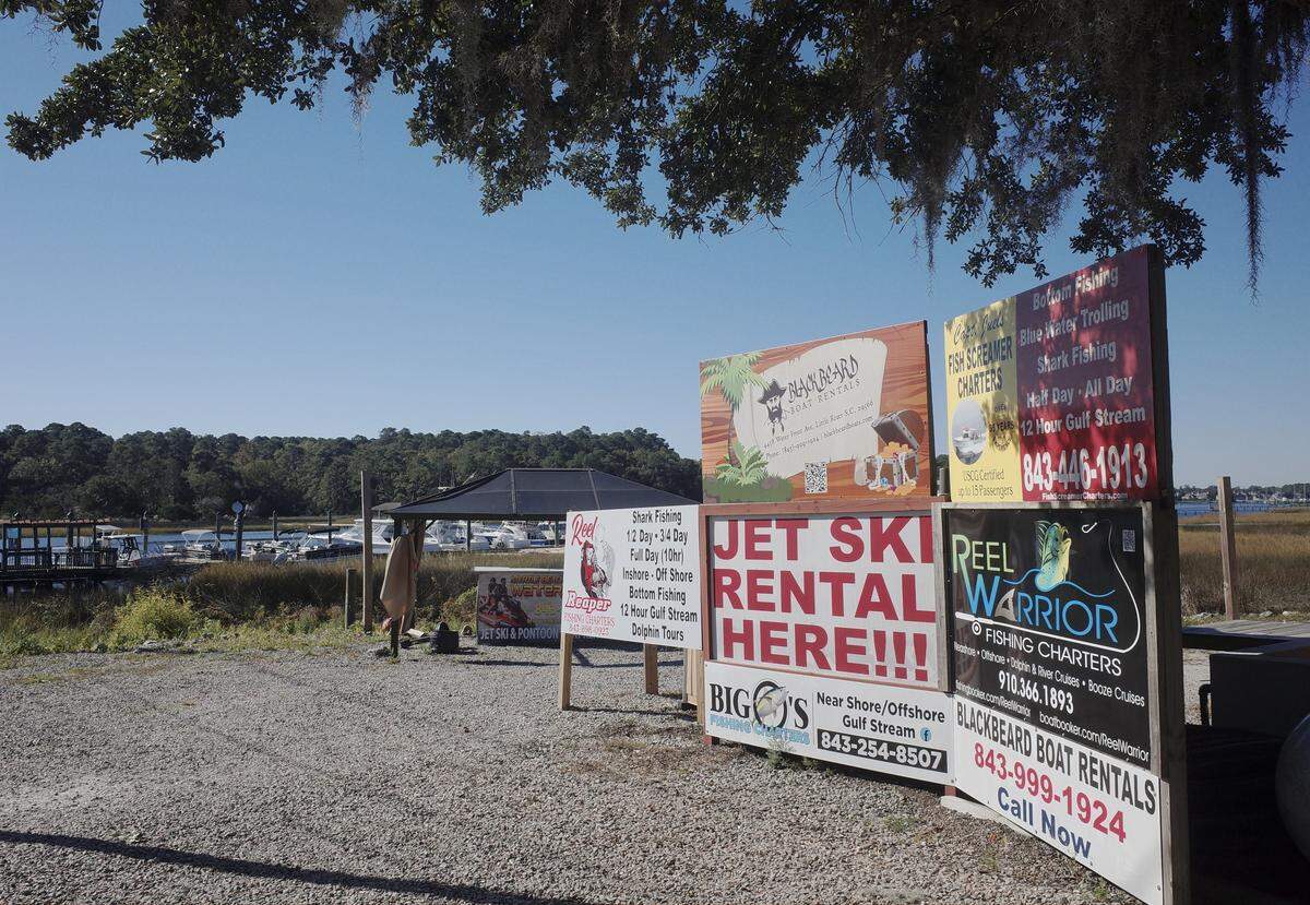 Fishing charter services and boat rental businesses advertise in the parking lot next to Crab Catchers restaurant on the Little River, SC waterfront. Tuesday, Oct.21, 2025.