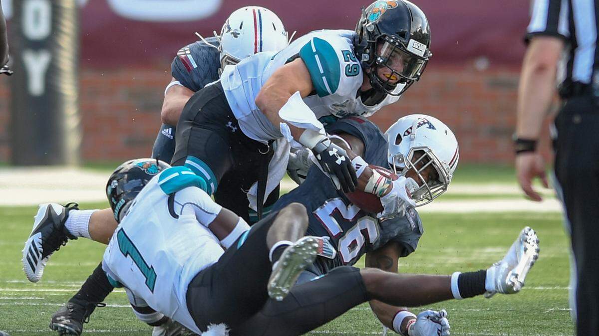 Coastal Carolina linebacker Silas Kelly (29, top) and defensive back Jave Brown (1) tackle Troy running back B.J. Smith during a game is 2018.