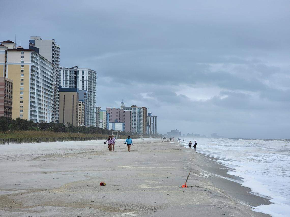 People walk along the shore in downtown Myrtle Beach between bands of rain in Tropical Storm Debby.