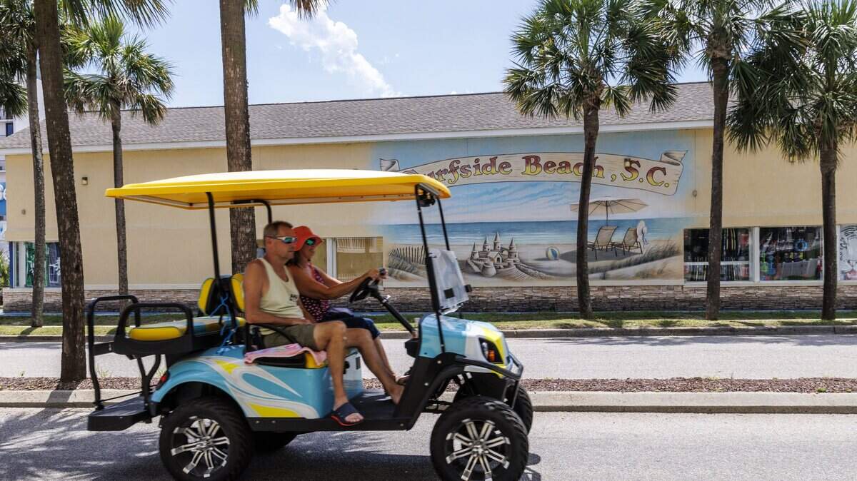 Golf cart riders pass a Surfside Beach mural on Surfside Drive on Monday. Surfside Beach council members are to voting to decide if golf carts will be allowed to be driven after dark on Surfside roads. Aug. 25, 2025.
