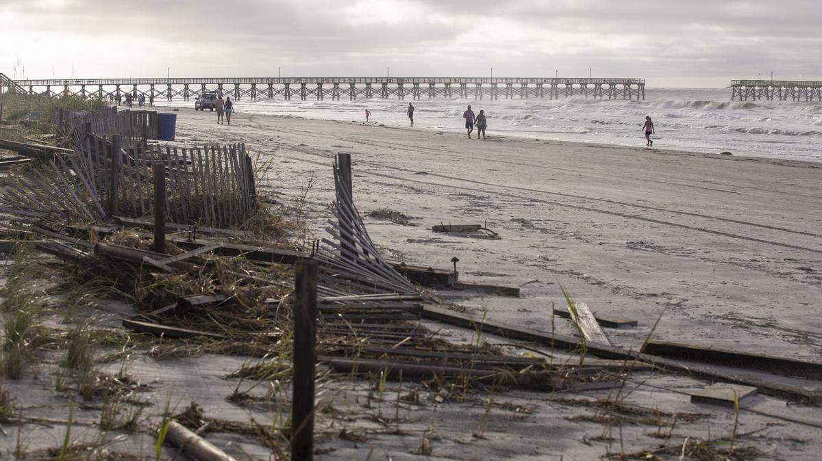 People walk Cherry Grove Point at dawn looking at debris scattered by Hurricane Isaias. Flooding and storm surge from Hurricane Isaias damaged docks in the Cherry Grove area canals and left a debris field on the beach in North Myrtle Beach after a section of pier collapsed and sand dune walkways were destroyed. August 4, 2020.