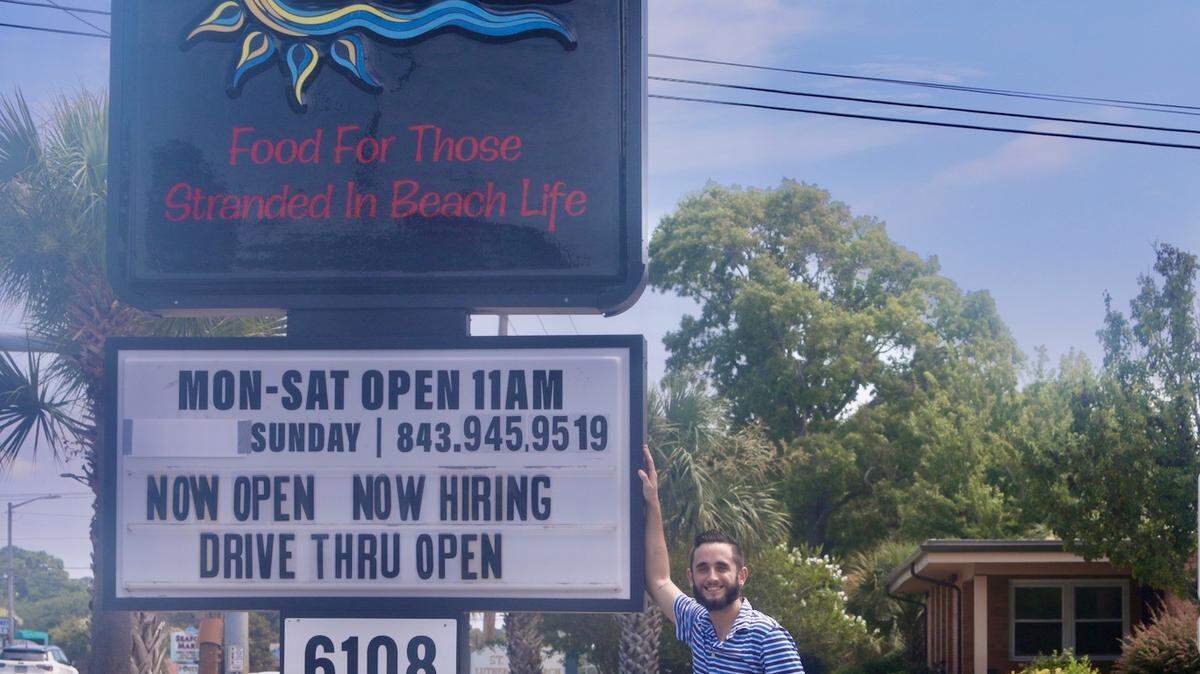 Dylan Ferguson, owner and operator of BEACHED, standing in front of his sign on North Kings Highway