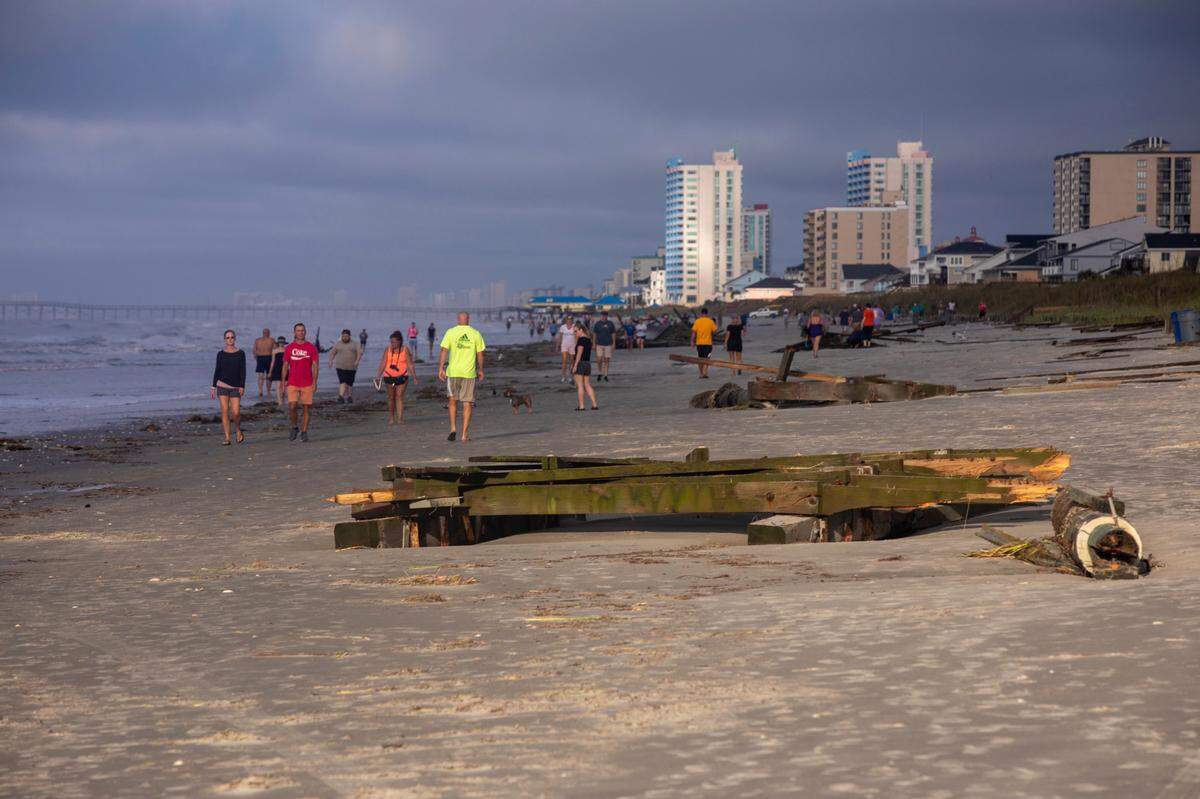 People walk Cherry Grove Point at dawn looking at debris scattered by Hurricane Isaias. Flooding and storm surge from Hurricane Isaias damaged docks in the Cherry Grove area canals and left a debris field on the beach in North Myrtle Beach after a section of pier collapsed and sand dune walkways were destroyed. August 4, 2020.