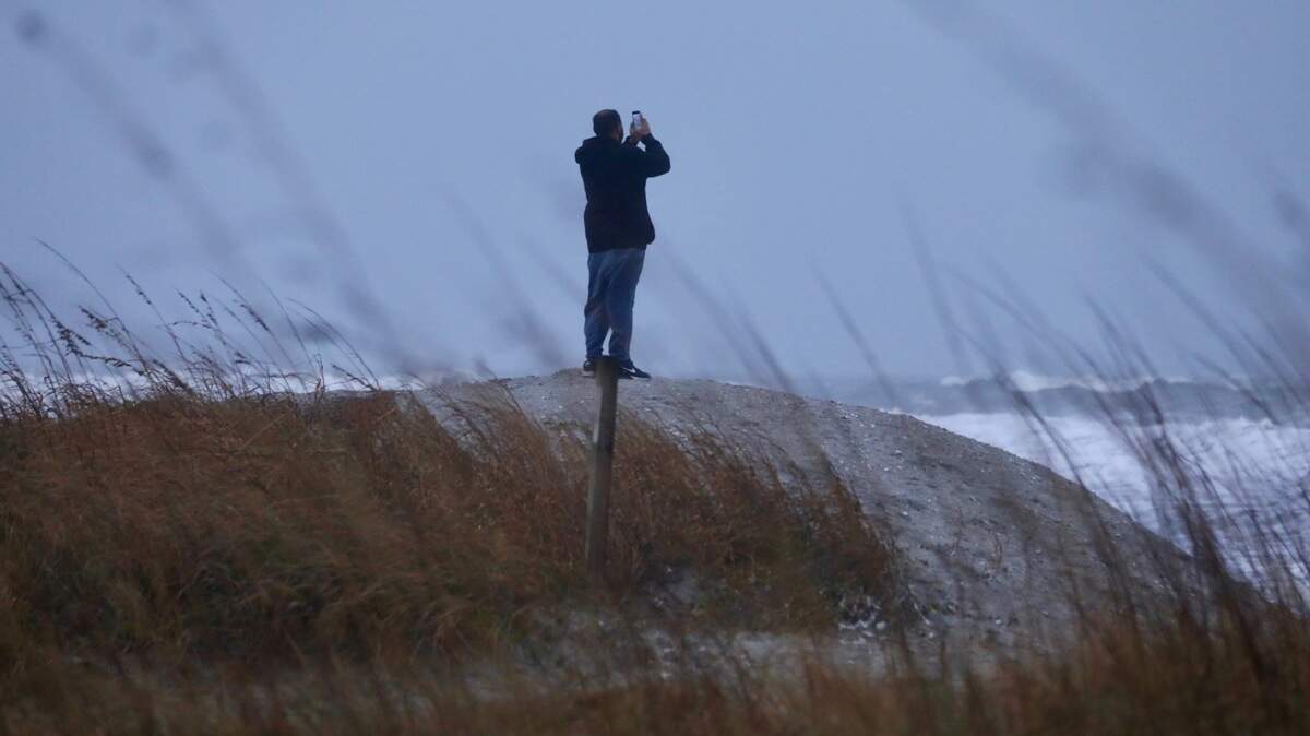 A man stands on a dune to photograph high surf in North Myrtle Beach, SC, Tuesday. North Myrtle Beach received wind gusts of up to 62 mph. Jan. 9, 2024