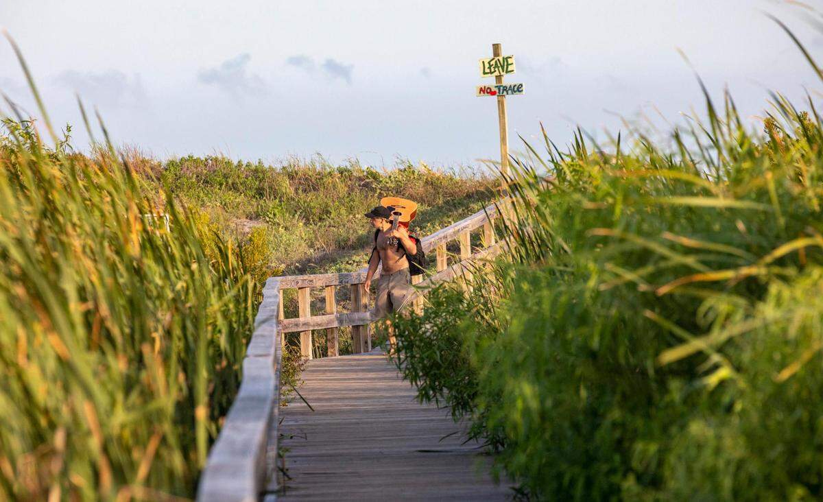 A beachgoer walks a long stretch of boardwalk crossing expansive dunes from Sullivan’t Island, S.C. Shifting sands are having opposite effects on some Charleston area beaches with erosion claiming the Folly Beach shoreline while Sullivan Island’s beach is growing. July 21, 2022.