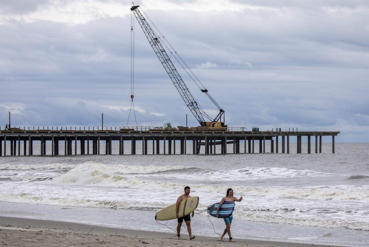 Surfers walk the beach past the Springmaid Pier that is currently being reconstructed after facing severe damage from Hurricane Matthew in 2017. Thursday. April 30, 2020