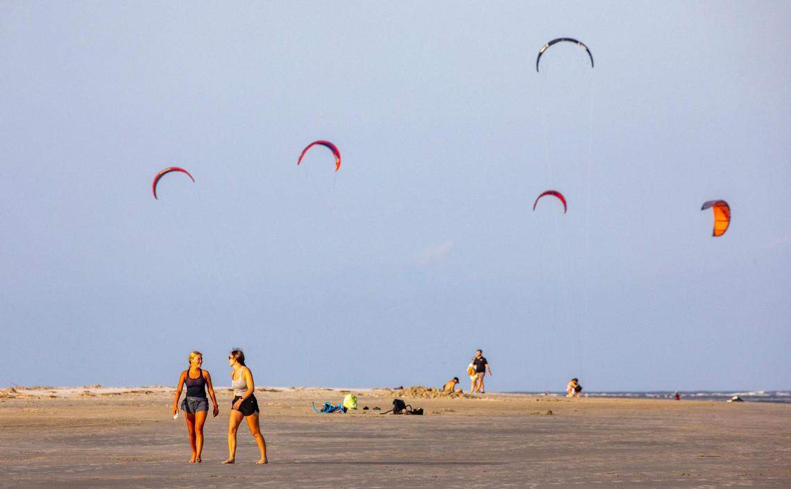 Beachgoer walk the broad expanse of the Sullivan’s Island beach front as kiteboarder’s sails fly in the distance. Shifting sands are having opposite effects on some Charleston area beaches with erosion claiming the Folly Beach shoreline while Sullivan Island’s beach is growing. July 21, 2022.