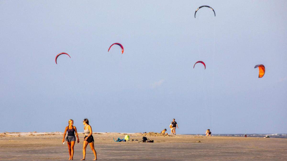 Beachgoers walk the broad expanse of the Sullivan’s Island beach front as kiteboarder’s sails fly in the distance. Shifting sands are having opposite effects on some Charleston area beaches with erosion claiming the Folly Beach shoreline while Sullivan Island’s beach is growing. July 21, 2022.