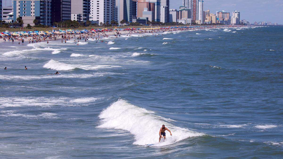 A surfer catches a wave near the Springmaid Pier with the city of Myrtle Beach skyline in the background. Myrtle Beach is home to several surf schools instructing surfers of all skill levels. TSN July 2, 2024 File.