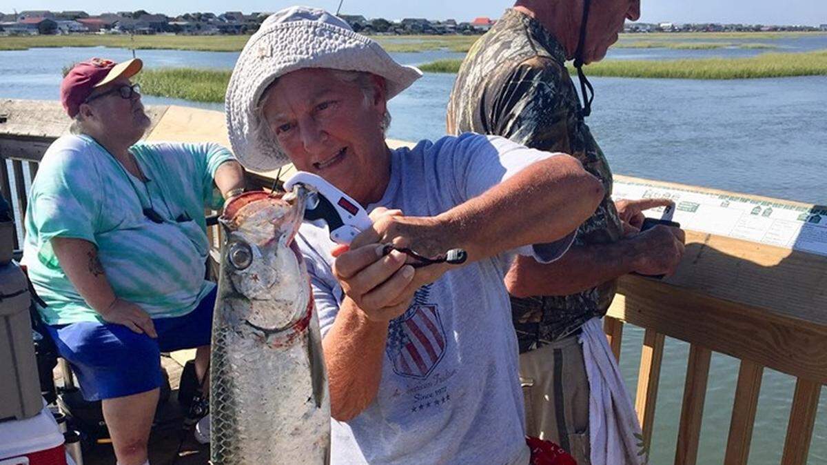 Judy Klopp handles a 24-inch tarpon caught off the boardwalk in Garden City Beach early this week, with her husband, Bill, in the background. The Klopps, part-time residents of Surfside Beach, released the juvenile tarpon.