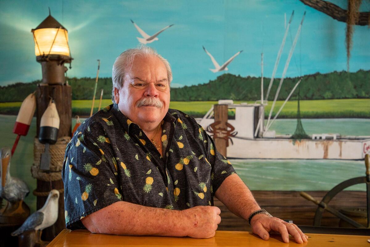 Joe Robertson, owner of Capt. Juel’s Hurricane restaurant, sits in front a a mural on the wall of his iconic eatery. The restaurant on the Little River waterfront is celebrating it’s 75th year of operation. March 11, 2020.