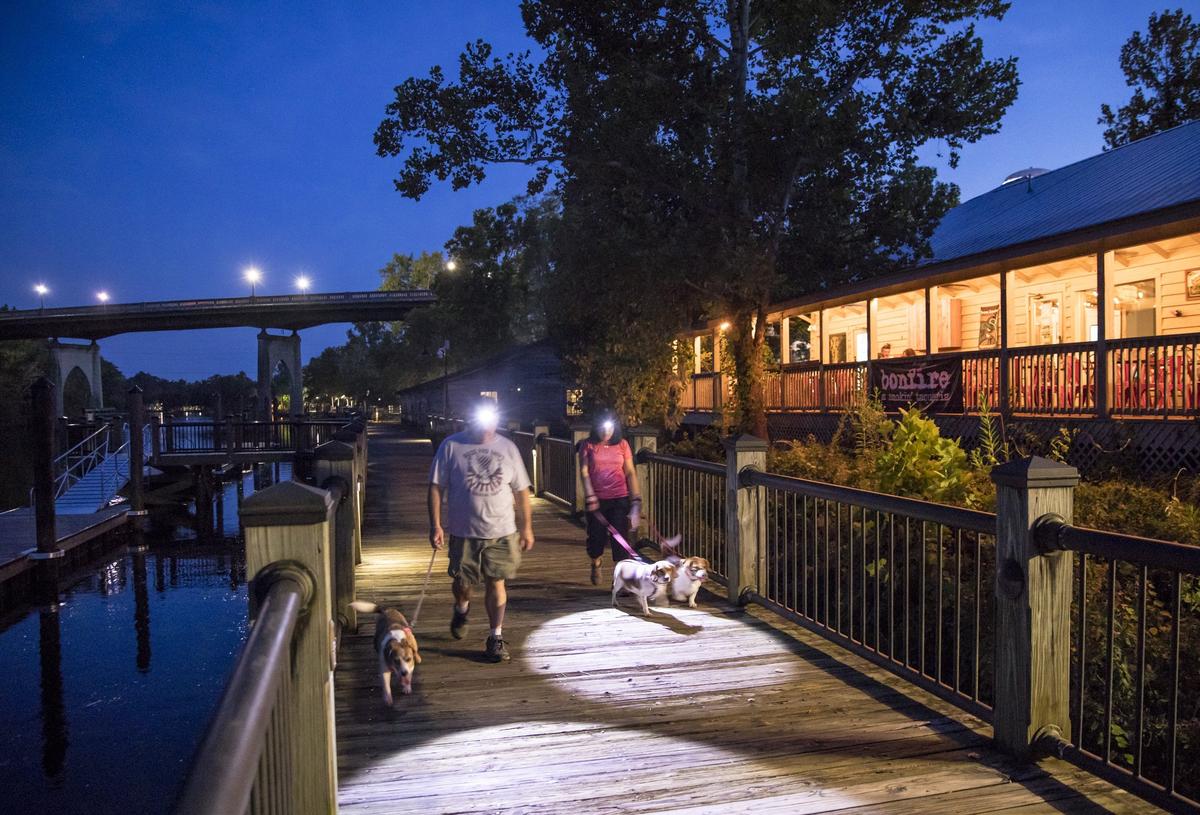 Michael and Aissa Richards walk their dogs Sassy, Sadie and Cena on Conway’s Riverwalk past the Bonfire restaurant on Thursday evening. Aug, 16 2018.