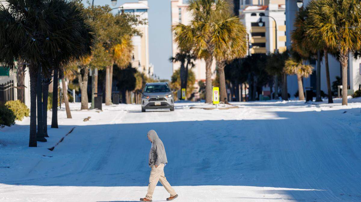 A man crosses an ice and snow covered Ocean Boulevard. Myrtle Beach residents and visitors were out enjoy a rare snow day on Wednesday after inches of snow covered the Grand Strand overnight. Jan. 22, 2025