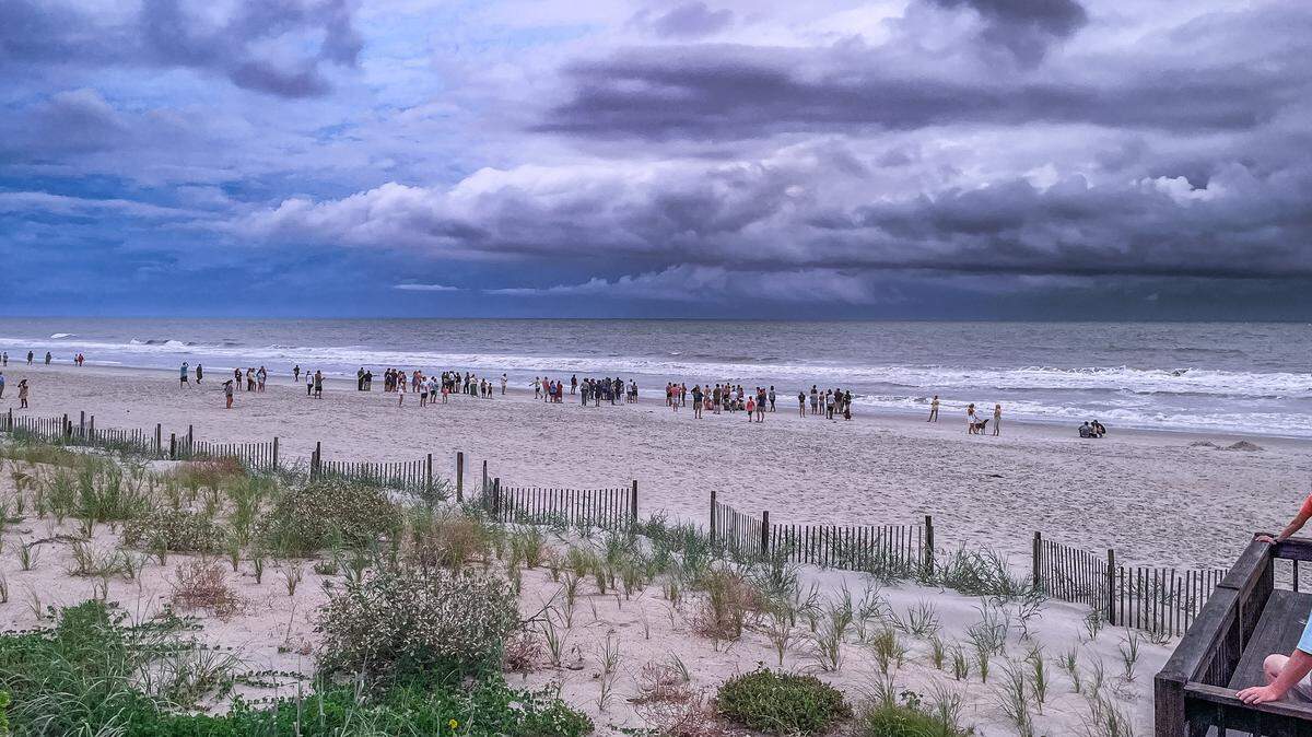 People stand on the beach in Pawleys Island as rescue crews search for a missing teen swimmer. The teen went missing in the surf Friday, July 12, 2024.