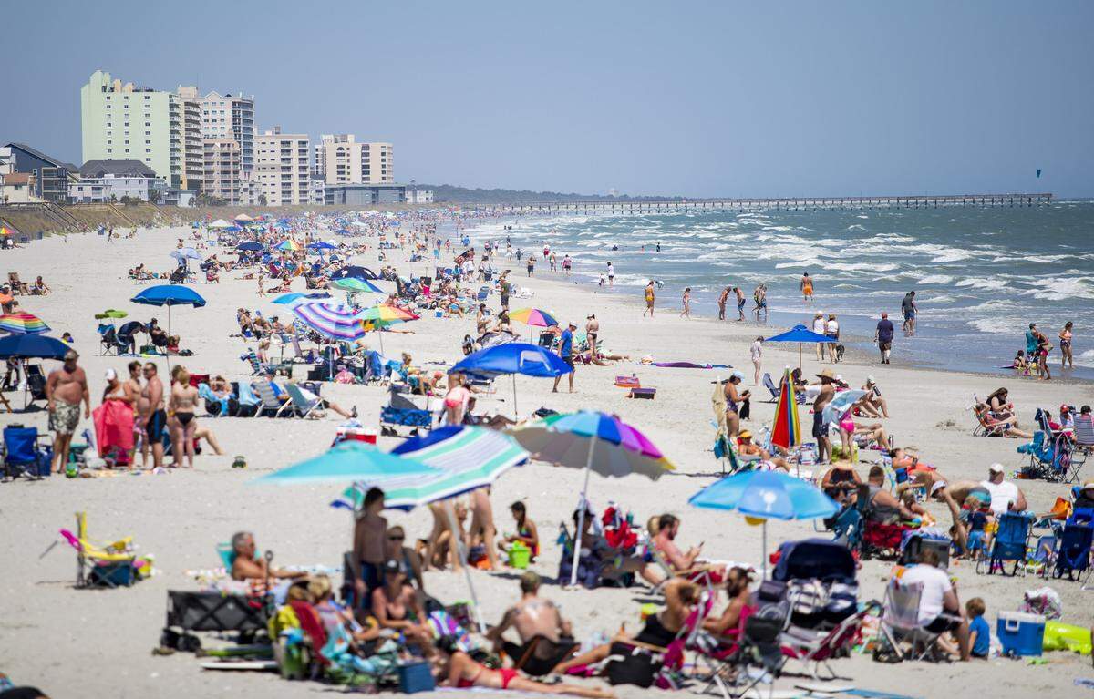 People sit along the beach near the Cherry Grove Pier Sunday afternoon in Cherry Grove as Coronavirus cases continue to rise in Horry County with three additional cases and one new death, according to SC DHEC. South Carolina Governor Henry McMaster issued an Executive Order on April 20 to lift restrictions on public access points to beaches and allow some businesses to reopen.
