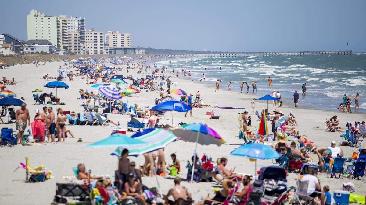 People sit along the beach near the Cherry Grove Pier Sunday afternoon in Cherry Grove as Coronavirus cases continue to rise in Horry County with three additional cases and one new death, according to SC DHEC. South Carolina Governor Henry McMaster issued an Executive Order on April 20 to lift restrictions on public access points to beaches and allow some businesses to reopen.